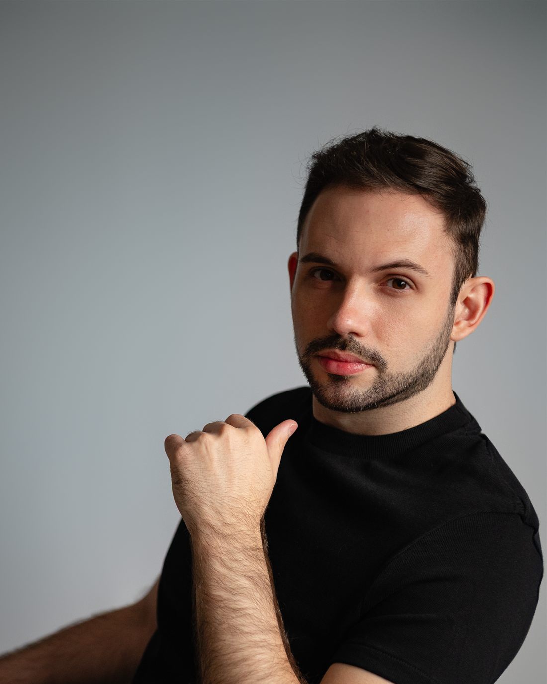 Leonardo Hermes, psicólogo, sentado em uma cadeira, olhando para a câmera, de camiseta preta sobre fundo claro